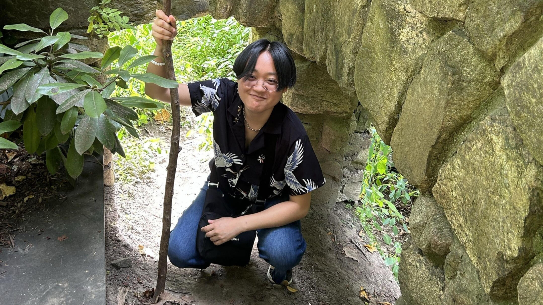 An Asian man crouching, holding a large stick.